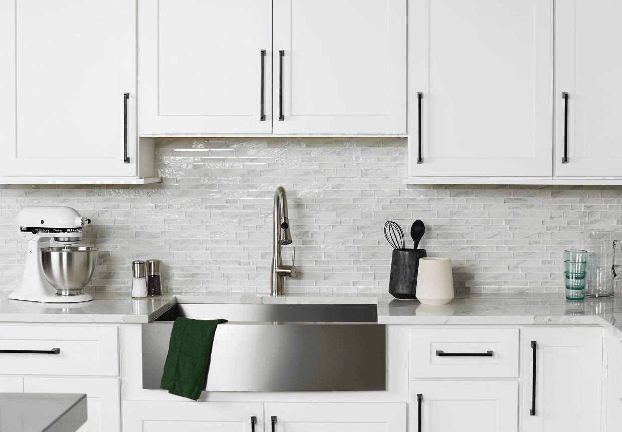 White shaker kitchen with black bar pulls, a stainless apron sink and a white glass tile backsplash